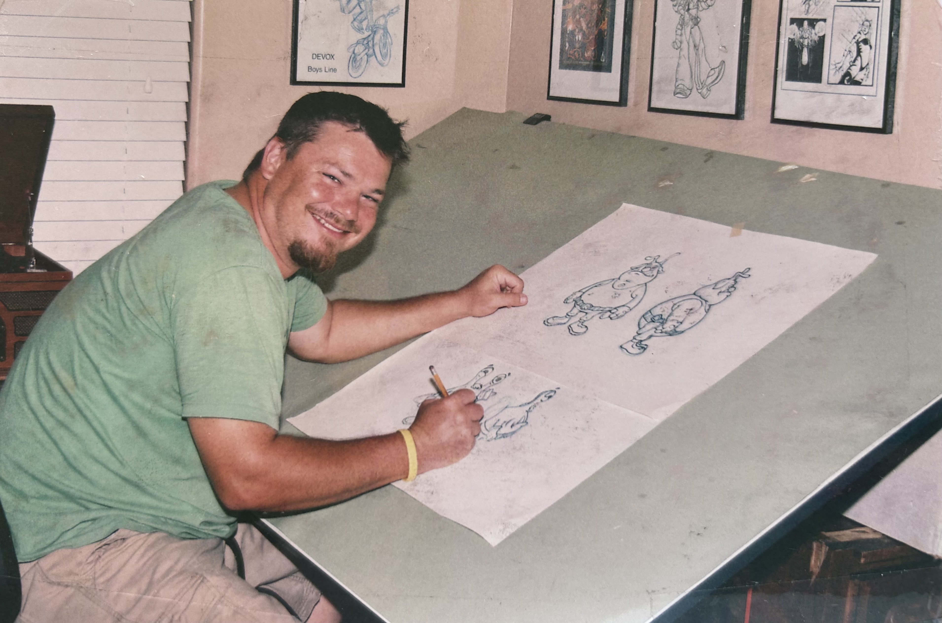 Josh Lakes sitting at a drafting desk with artwork